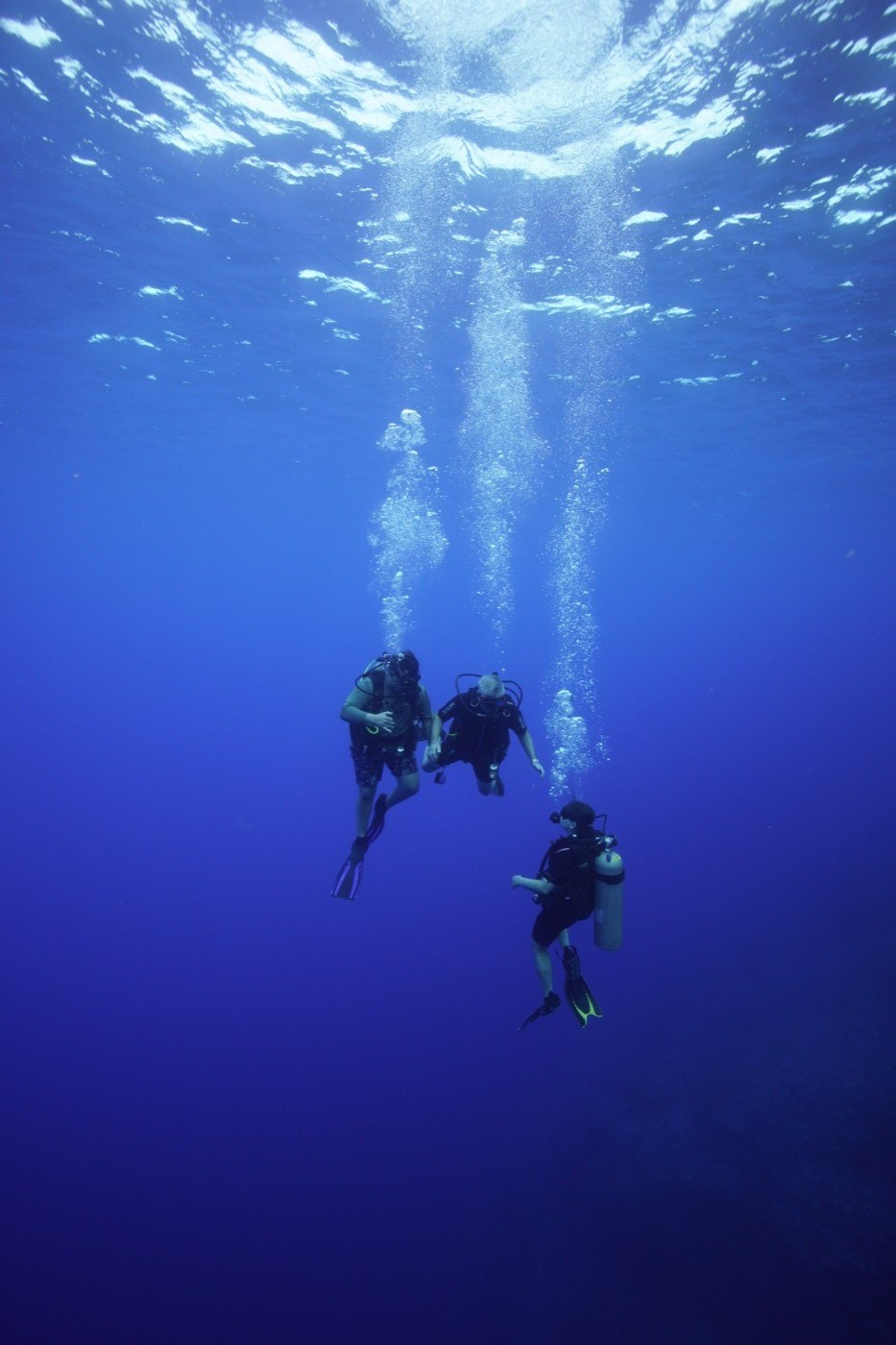 Three scuba divers underwater with bubbles rising to the surface