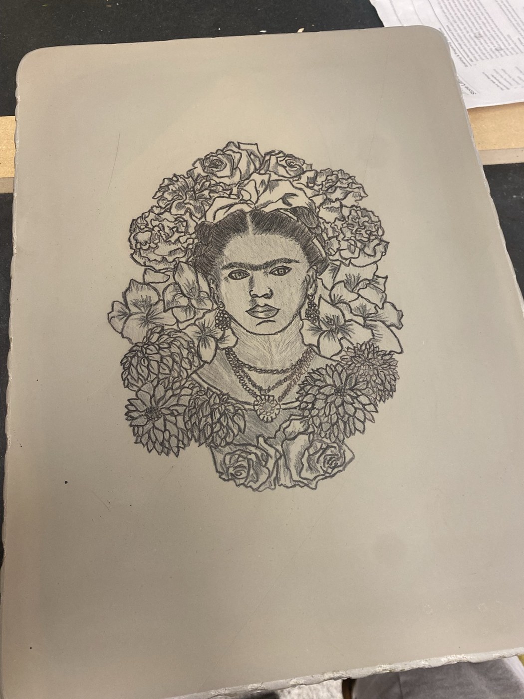 A pencil lithograph of Frida Kahlo surrounded by flowers, drawn on a litho plate